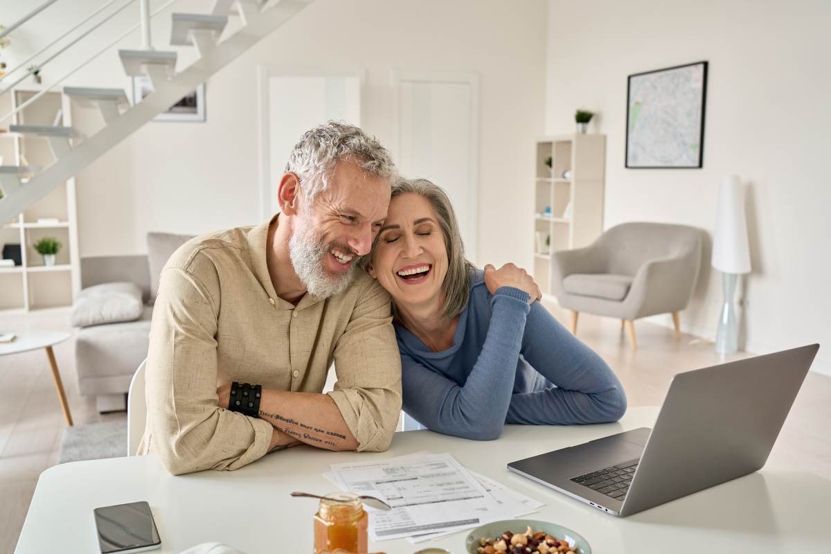 Mature couple smiling at kitchen table as they review their finances