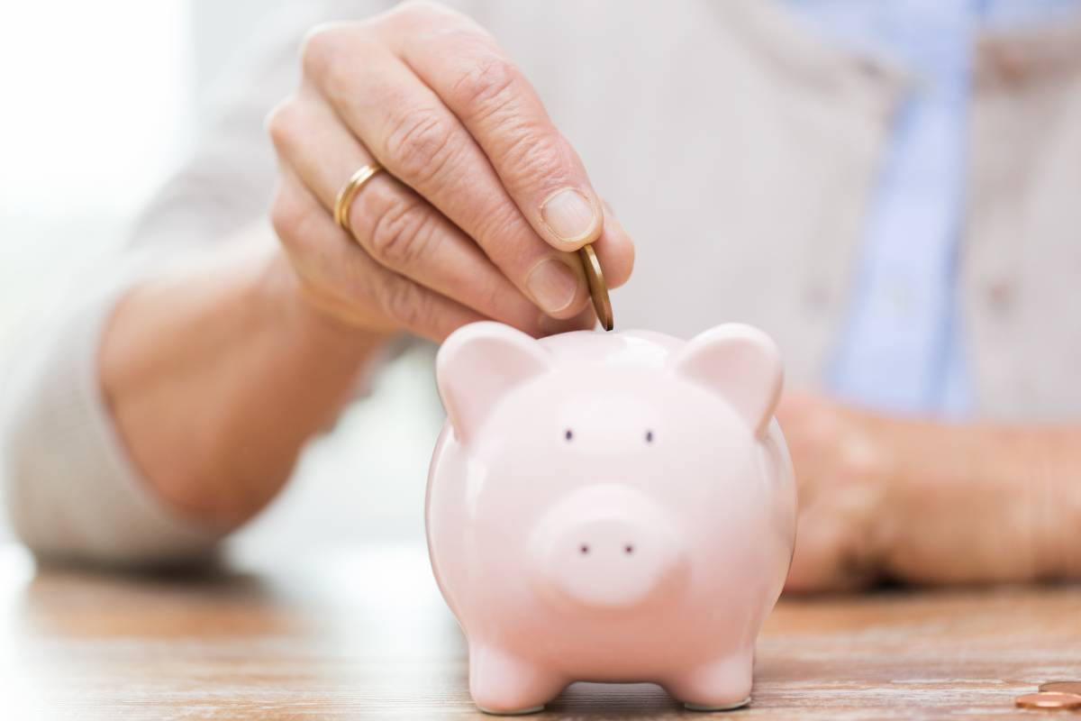 A hand putting money in a piggy bank.