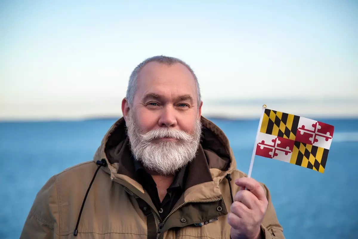 A man of retirement age holds a small Maryland state flag.