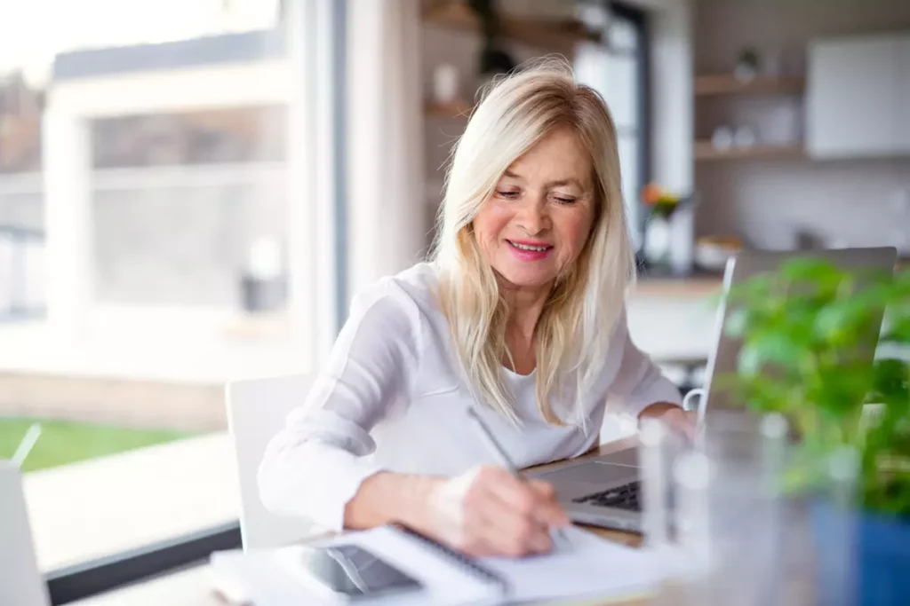 An older woman works from home in a sunny office.