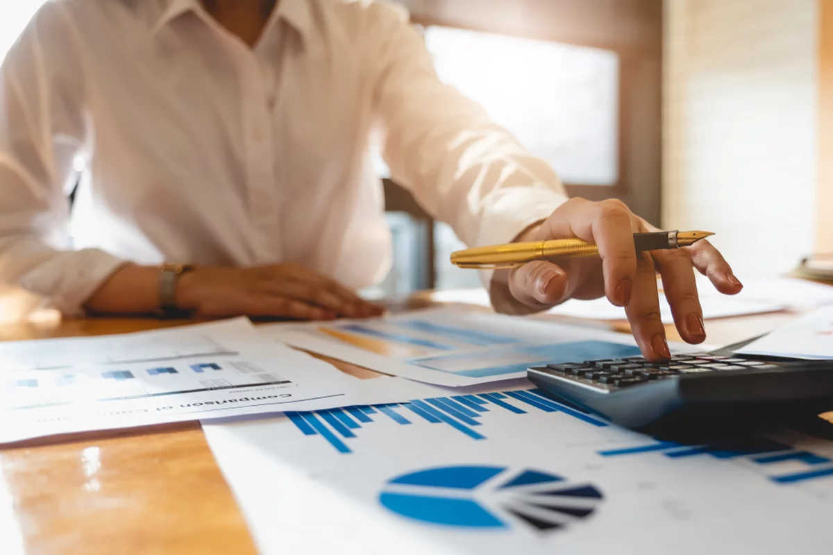 A businesswoman attempts to calculate her personal financial planning, paperwork, and calculator on her desk.