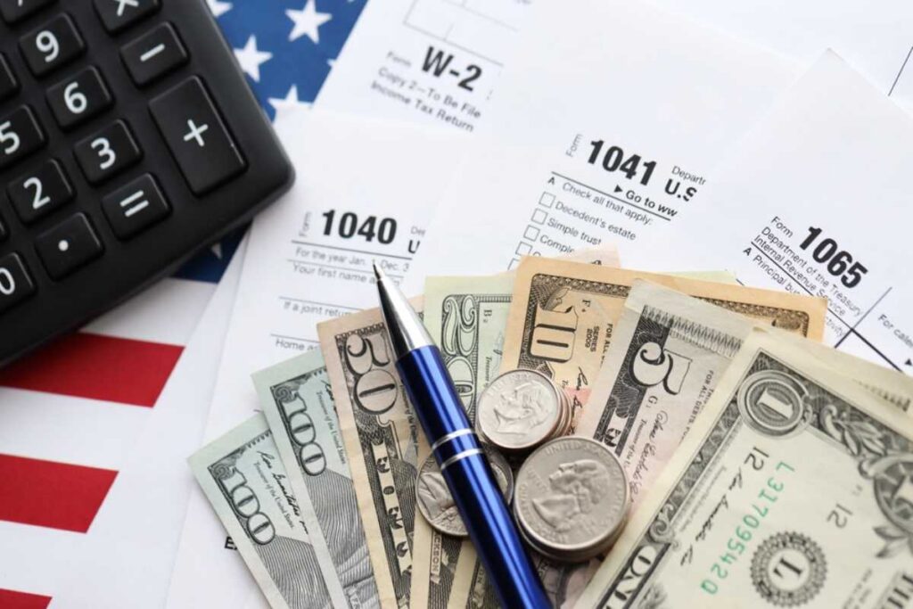 Tax forms, calculator, money, and a pen set atop an American flag background