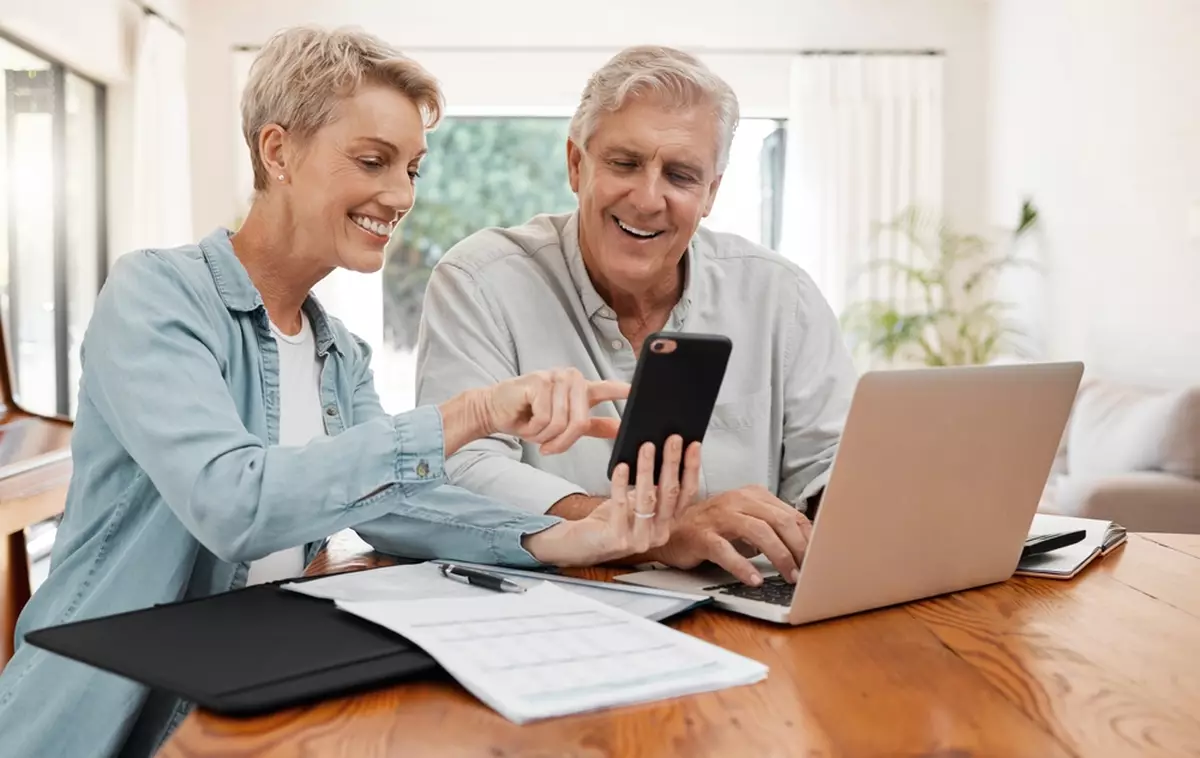 A senior couple going over their finances on their laptop and phone.